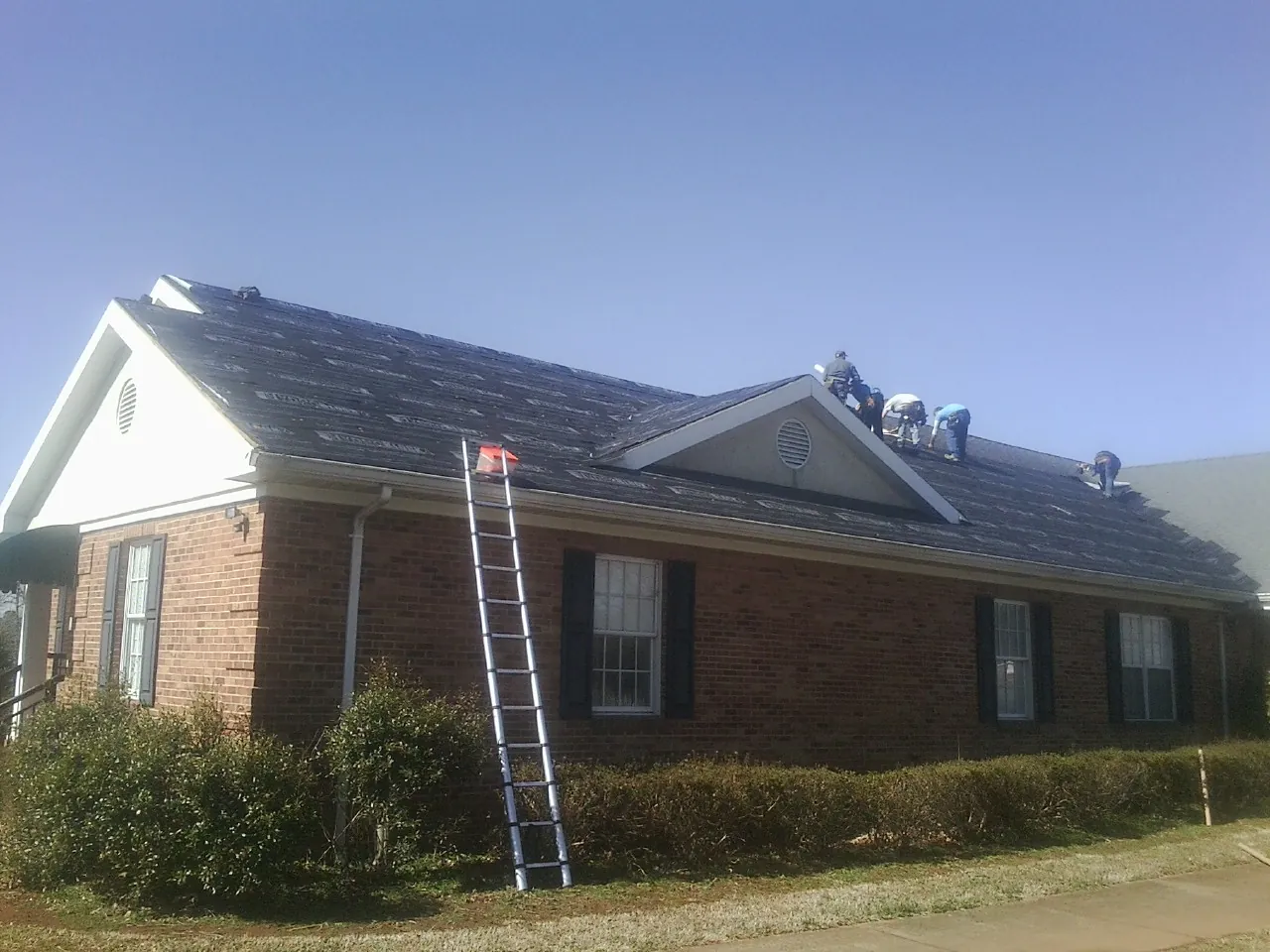 Crew tearing shingles off a brick ranch roof with a ladder set — Emergency Roof Repair work by our crew in Bryn Athyn