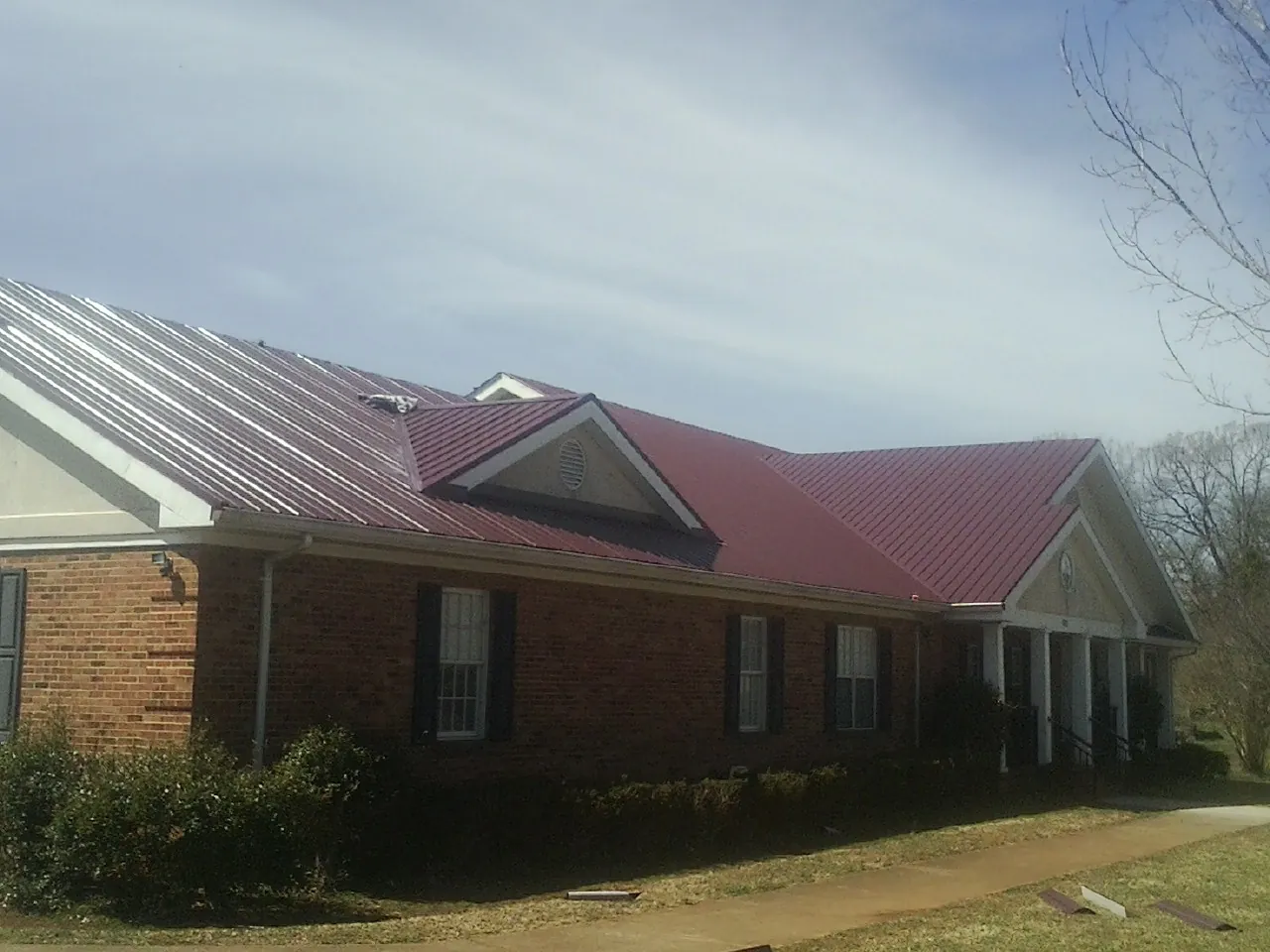 Red metal roof with gabled entries on a long brick building, from a Hail Damage Roof Repair job in Bryn Athyn