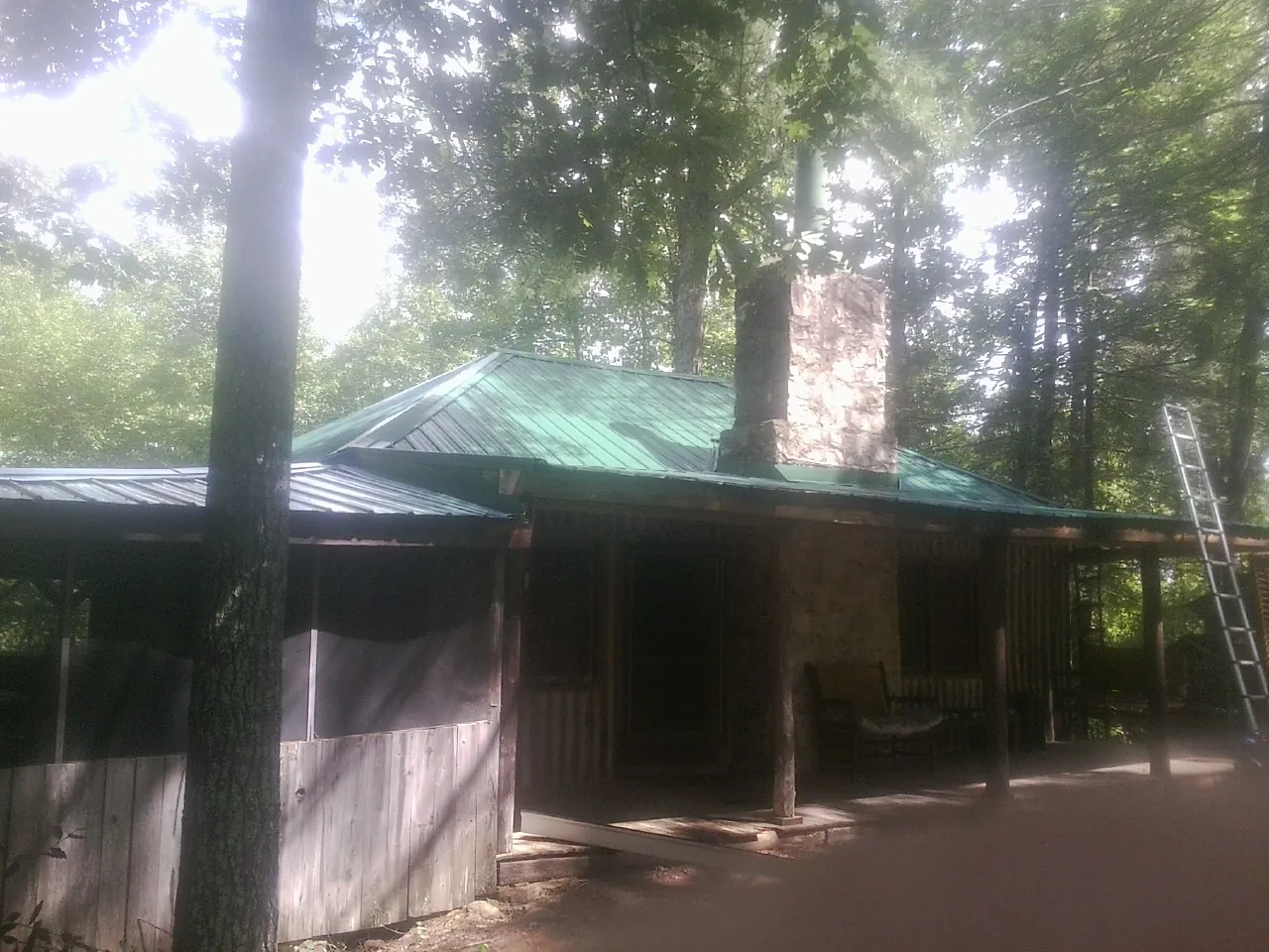 Green metal roof and stone chimney above a log cabin porch in Bryn Athyn
