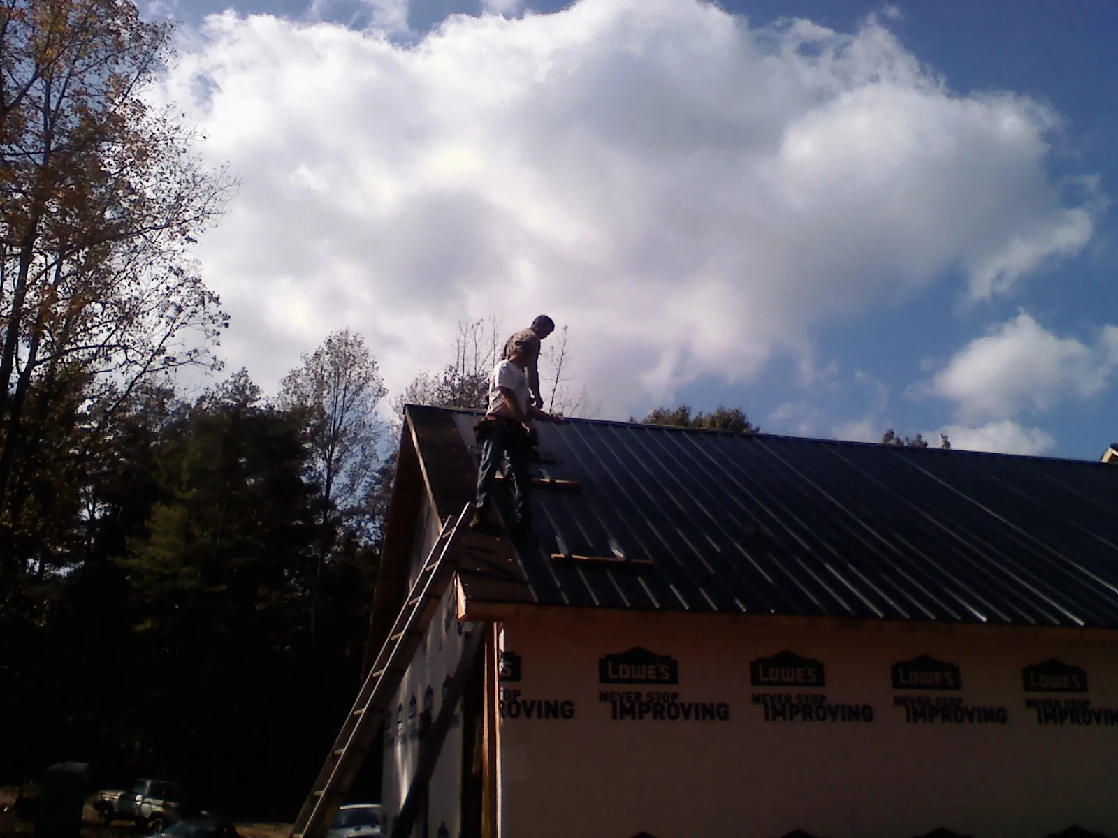 Roofer fastening dark metal panels high against a cloudy sky, from a Roof Inspection job in Bryn Athyn