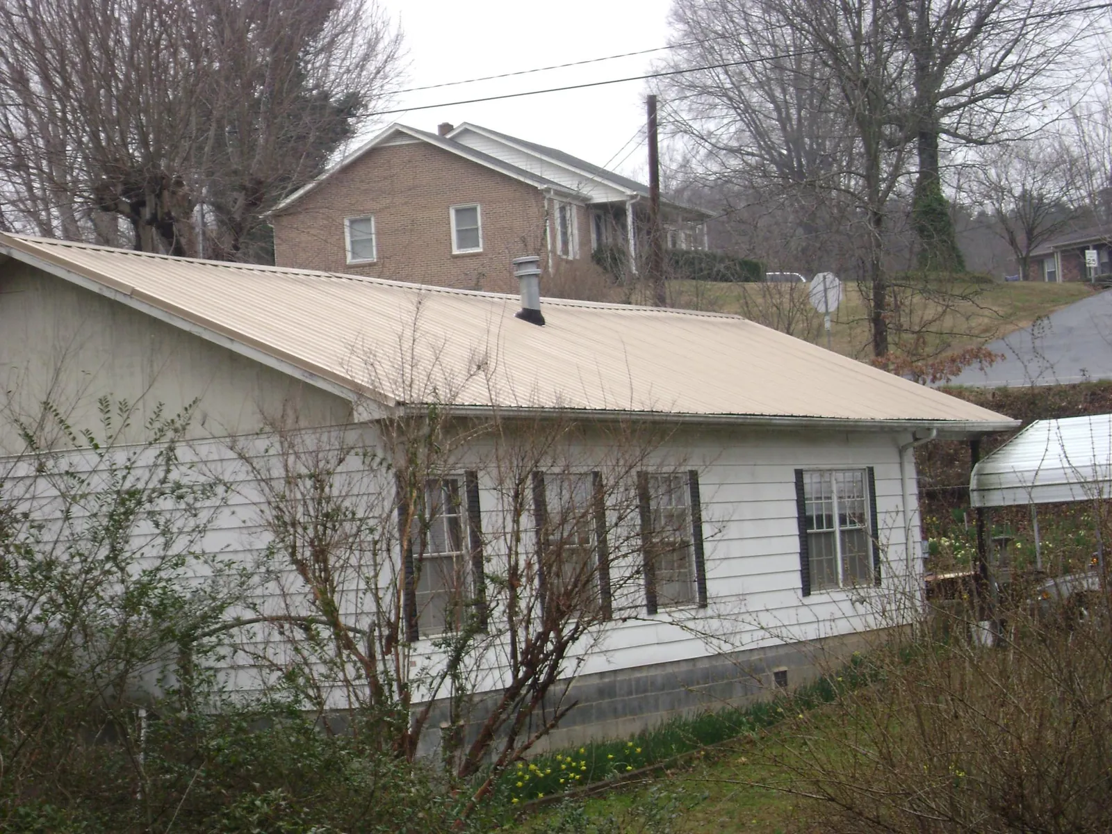 Tan metal roof on a white sided house set into a hillside — Commercial Roofing by Roofing Brothers in Bryn Athyn
