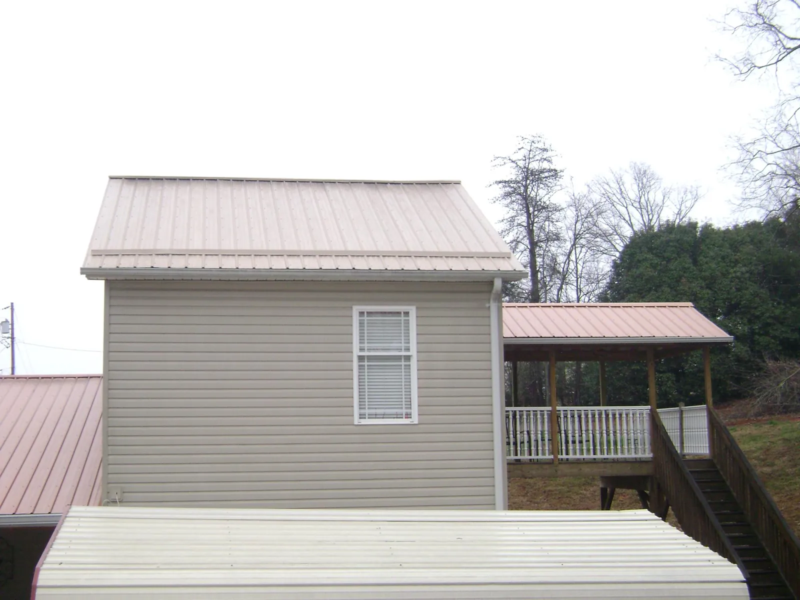 Tan metal roofs on a two story addition and attached porch, from a Roof Replacement job in Bryn Athyn